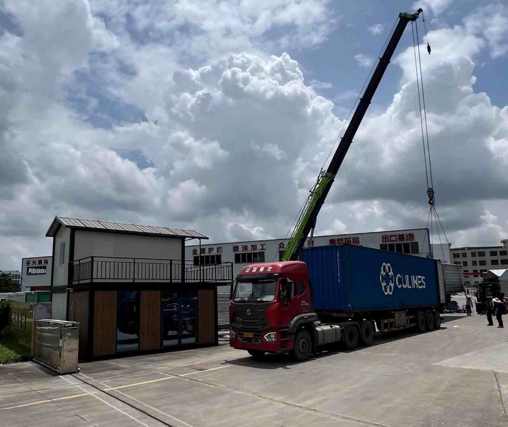 Crane loading modular container house onto shipping container at steel structure factory